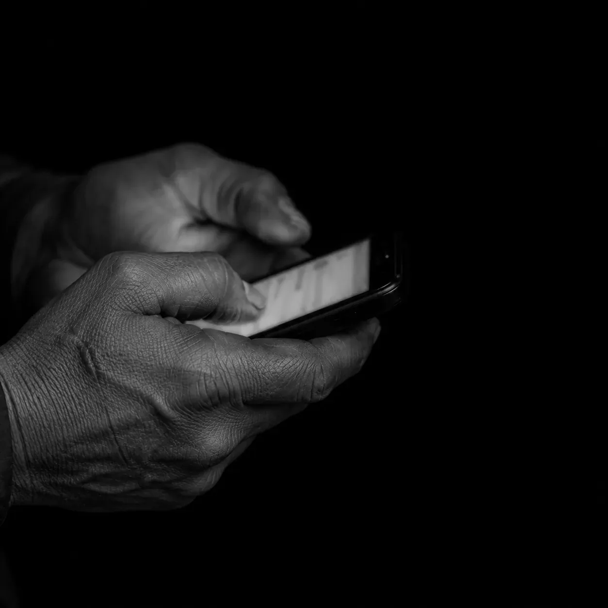 Worn hands holding a phone, the screen the only light, one red notification light lit.